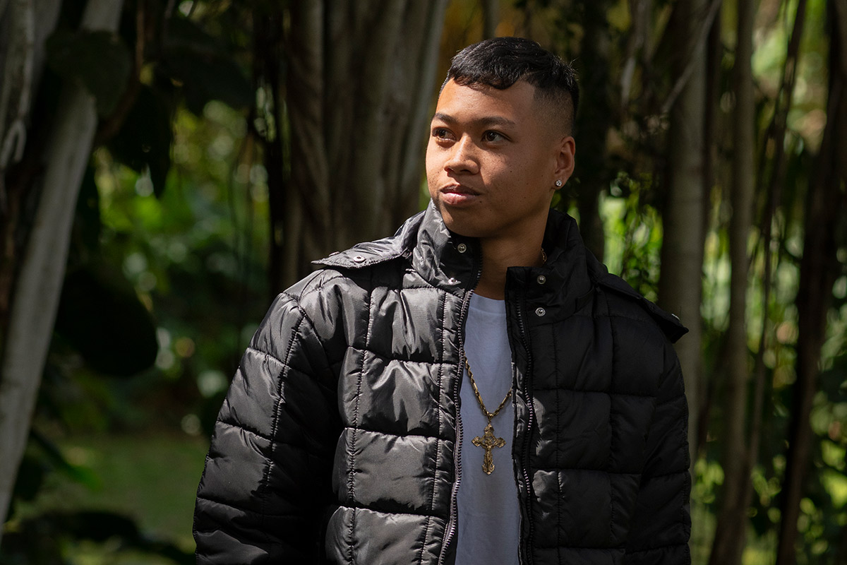 A teenage boy stands in a tropical forest and looks wistfully off to the distance.