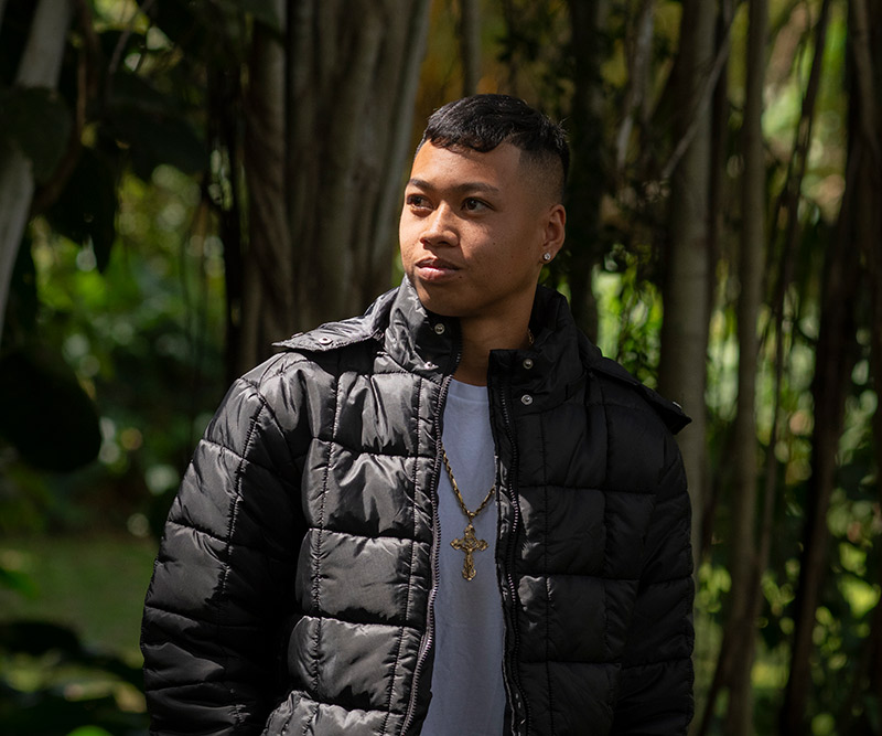 A teenage boy stands in a tropical forest and looks wistfully off to the distance.