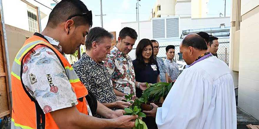 Straub leadership hold a long maile lei as a minister leads them in prayer.