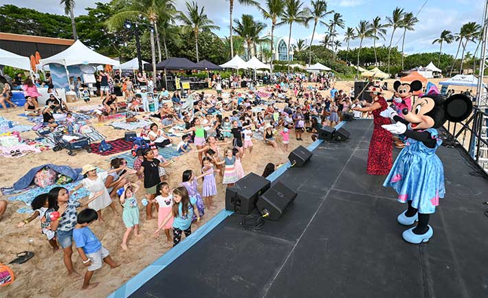 Characters actors as Mickey and Minnie Mouse on stage leading children in dance on the beach