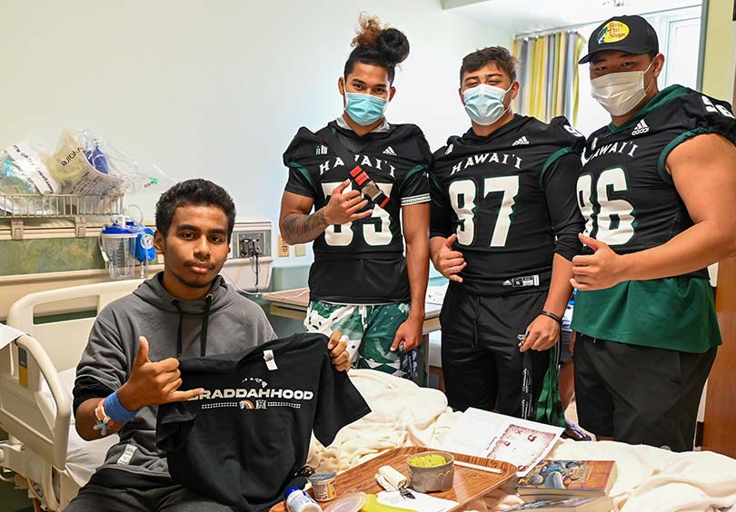 Football players in masks beside a young male patient all throwing shakas.