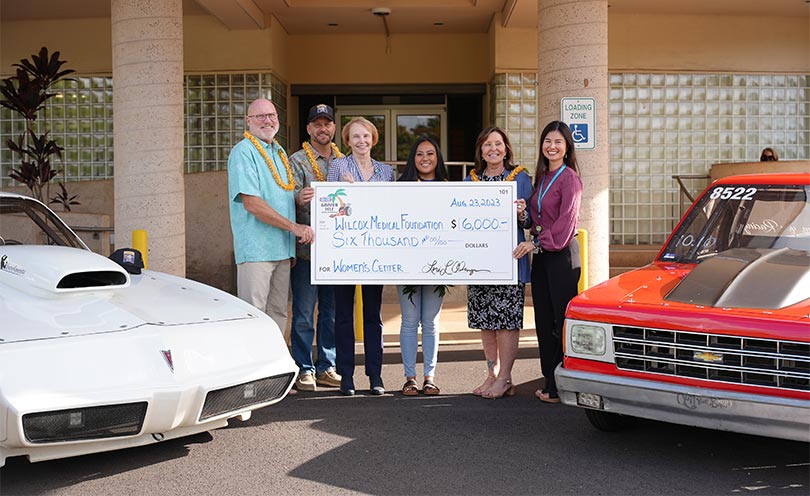 People flanked by drag racing cars holding giant check.