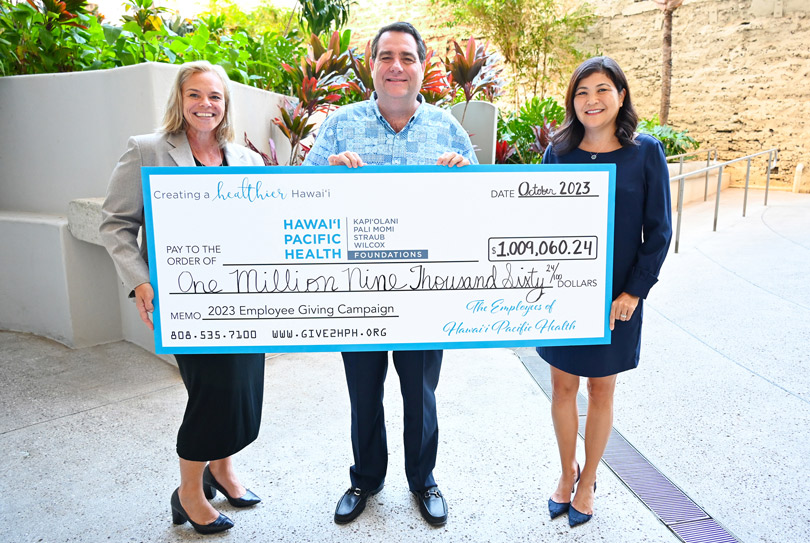 Two women and a man hold up a giant check