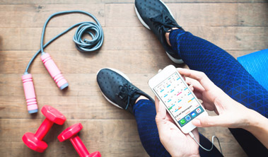 a woman sits on the ground next to a jump rope and dumbbells looking at a mammogram appointment on her cell phone screen