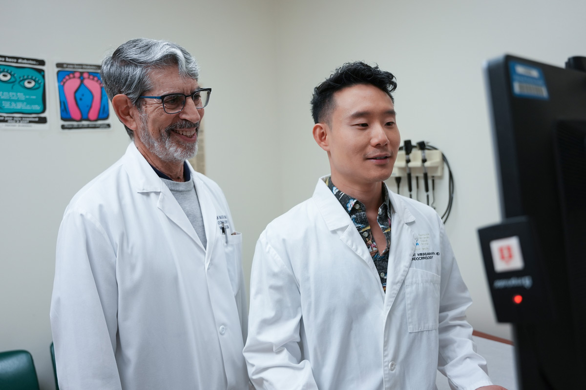 Two male doctors look at a computer screen in an exam room.