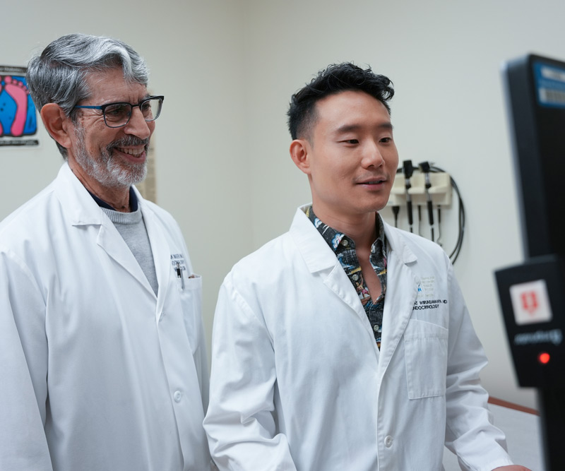 Two male doctors look at a computer screen in an exam room.