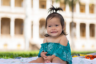 Smiling toddler with a ponytail on her head.