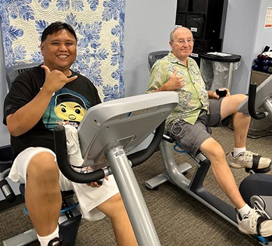 Young man and older man on stationary bikes.