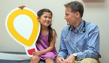 Young patient holding large Children's Miracle Network logo alongside her cardiologist.