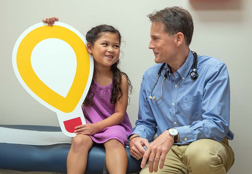 Young patient holding large Children's Miracle Network logo alongside her cardiologist.