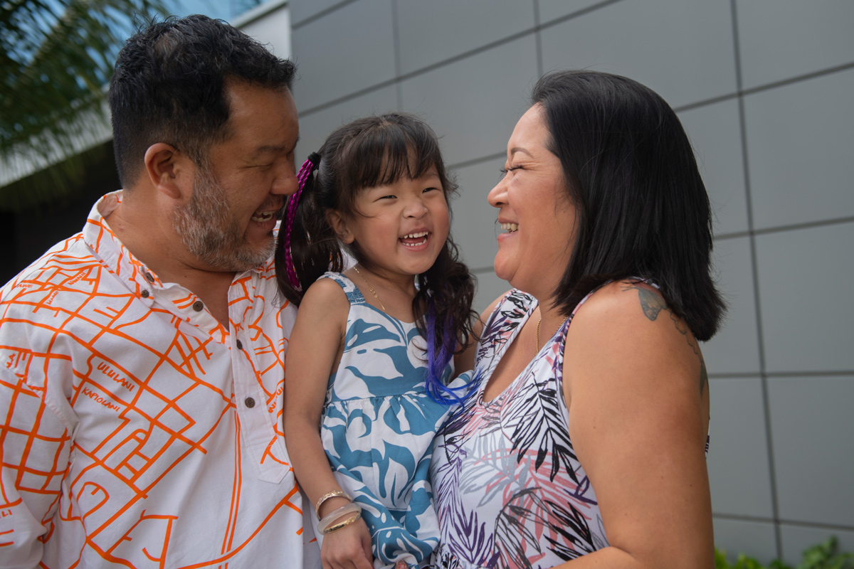 A man and woman hold their 4-year-old daughter and smile at each other.