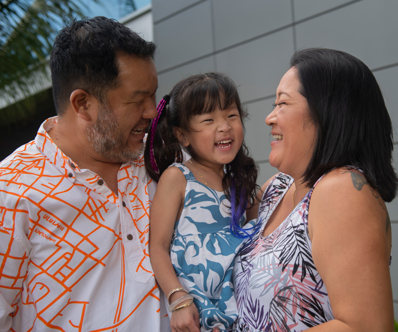 A man and woman hold their 4-year-old daughter and smile at each other.