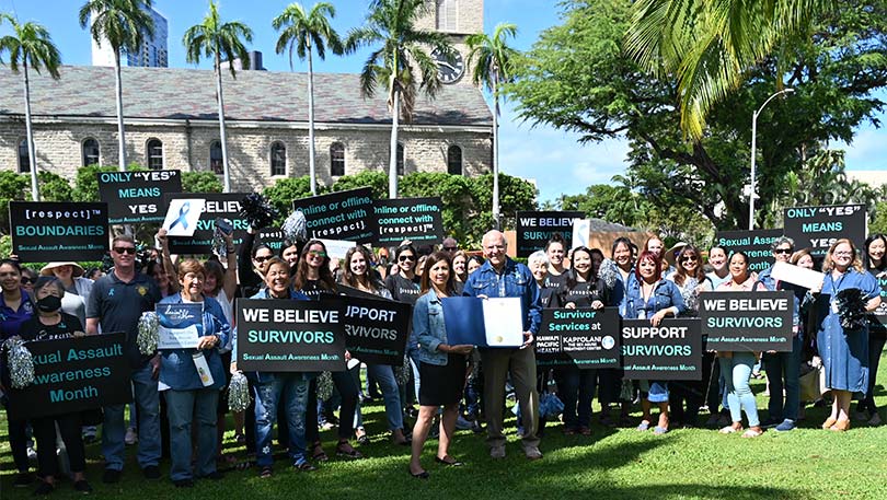 Large group shot of people wearing denim and holding signs in support of sexual assault awareness month.