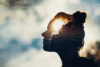 Silhouette of a woman's head superimposed over a calm body of water.