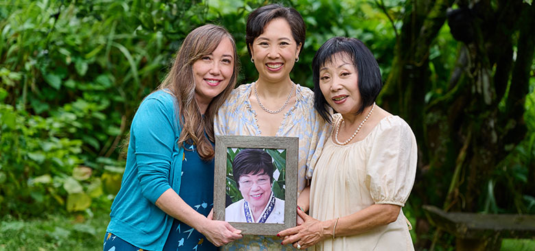 Three women standing closely together holding photo of a fourth.