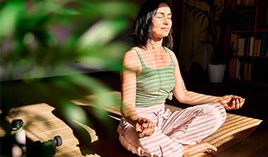 Woman meditating in a calm spot dappled in sunlight.