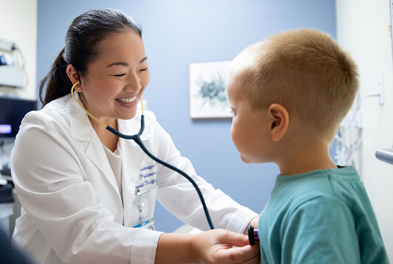 Smiling pediatrician listens to a young patient's heart and lungs.