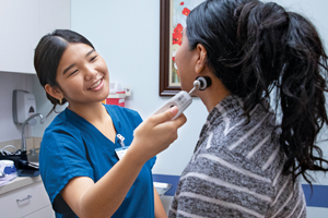 Smiling medical assistant with a patient in an exam room.