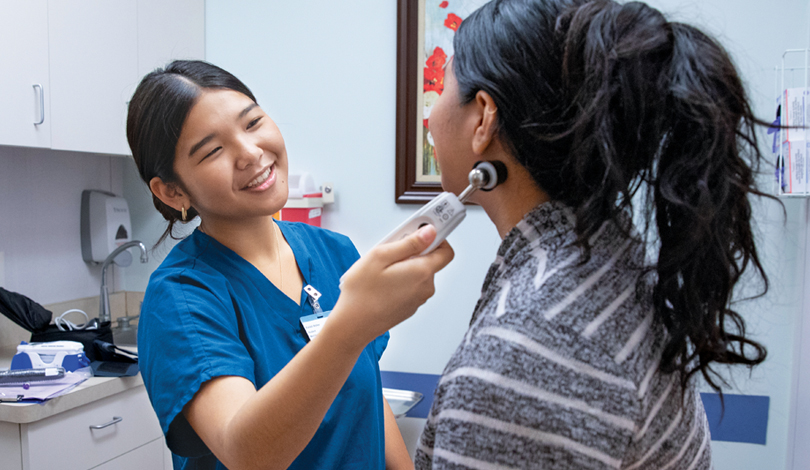 Smiling medical assistant with a patient in an exam room.