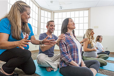 Class of seated pregnant women and their partners getting instruction in massage and breathing.