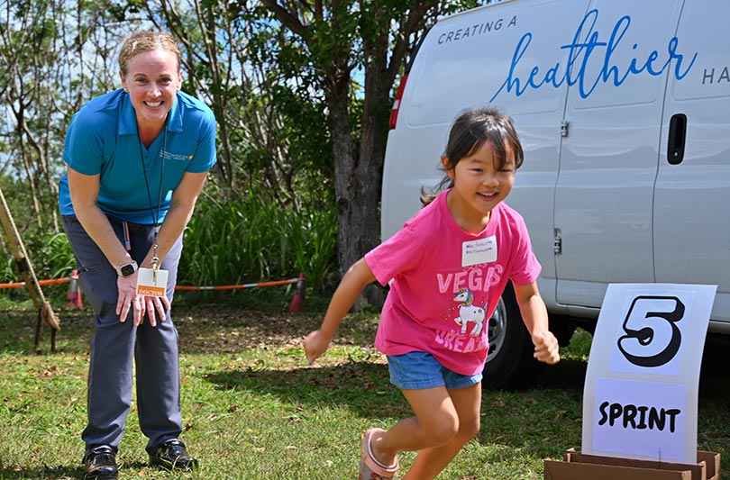 Smiling doctor looking on as young girl does a running activity.