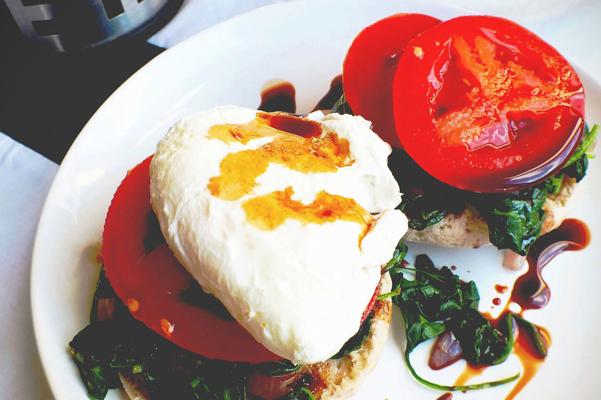 A poached egg sits on tomatoes and spinach on an english muffin.