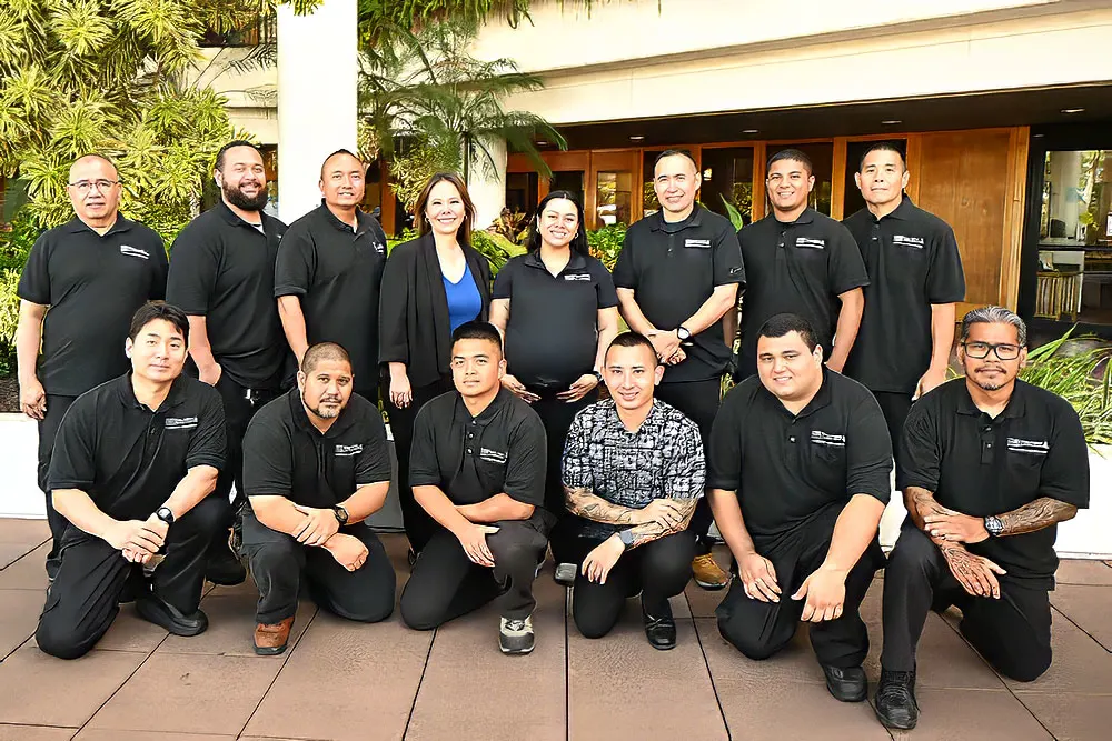 Large group with two rows of facilities staff in black polo shirts at Pali Momi Medical Center.