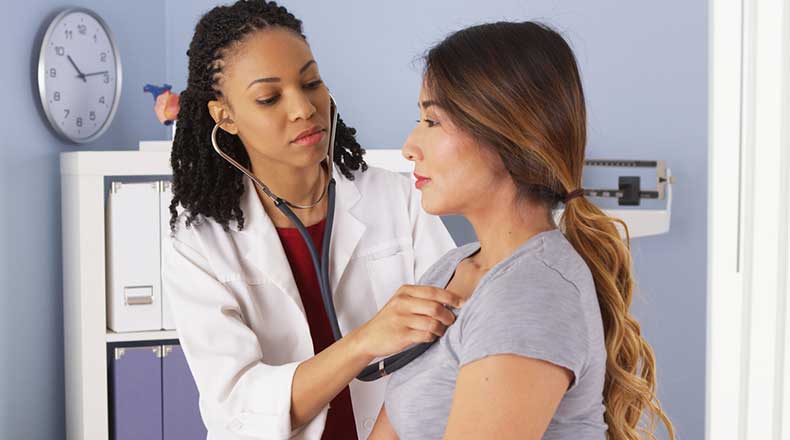 Doctor using stethoscope to listen to a woman's heart.
