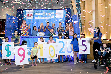 Children holding numbers showing $910,285 with confetti falling down and adults cheering