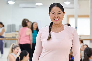 Smiling woman with braid and pink top in a fitness class.