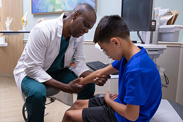 Doctor examines a young boy's arm and elborw.
