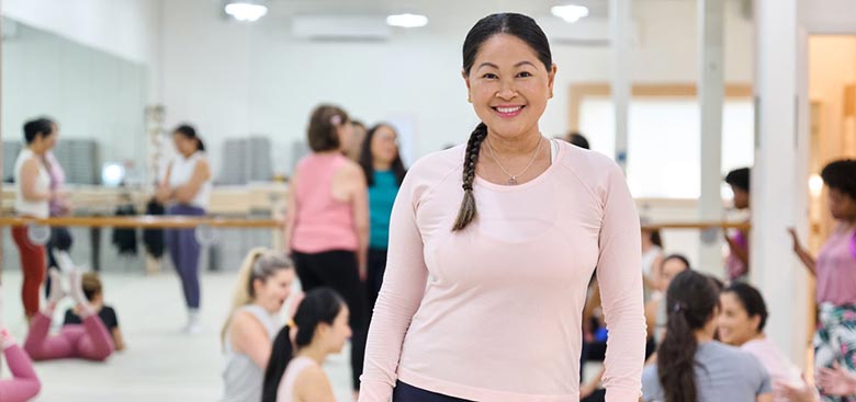 Portrait of a smiling woman in pink workout top at an exercise studio.