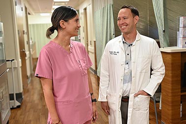 Doctor and colleague in pink scrubs in medical center hallway.