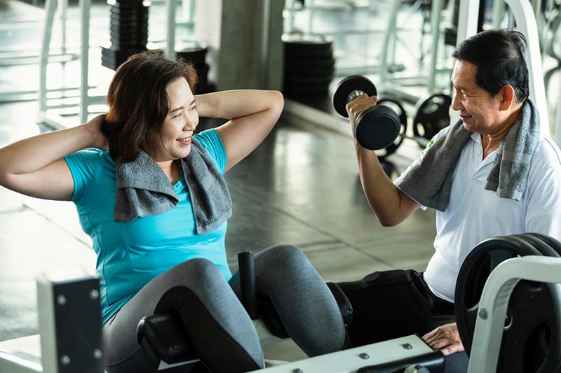 Woman on gym equipment alongside man lifting weights.