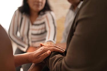 People sitting together with one person resting their hand on another's arm.