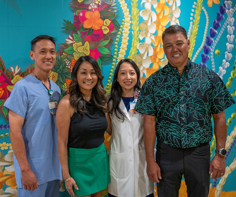 two men and two women stand in front of a wall mural of Hawaiian flowers