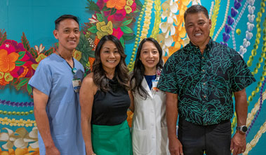 two men and two women stand in front of a wall mural of Hawaiian flowers