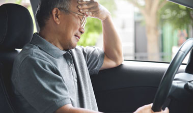 older man holds head while sitting in the driver's seat of a car
