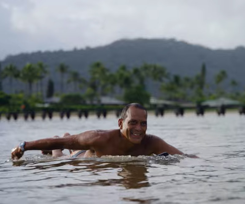a man paddles out to surf at Hanalei Bay on Kauai