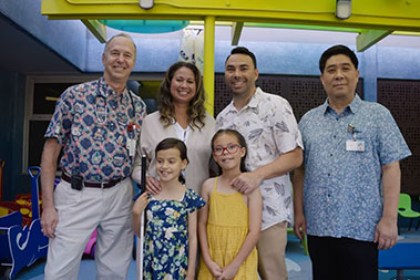 Family with doctors alongside their two young girls, one holding a mobility cane.