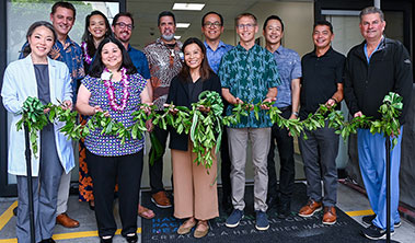 Large group of people in front of doorway holding very long maile lei.