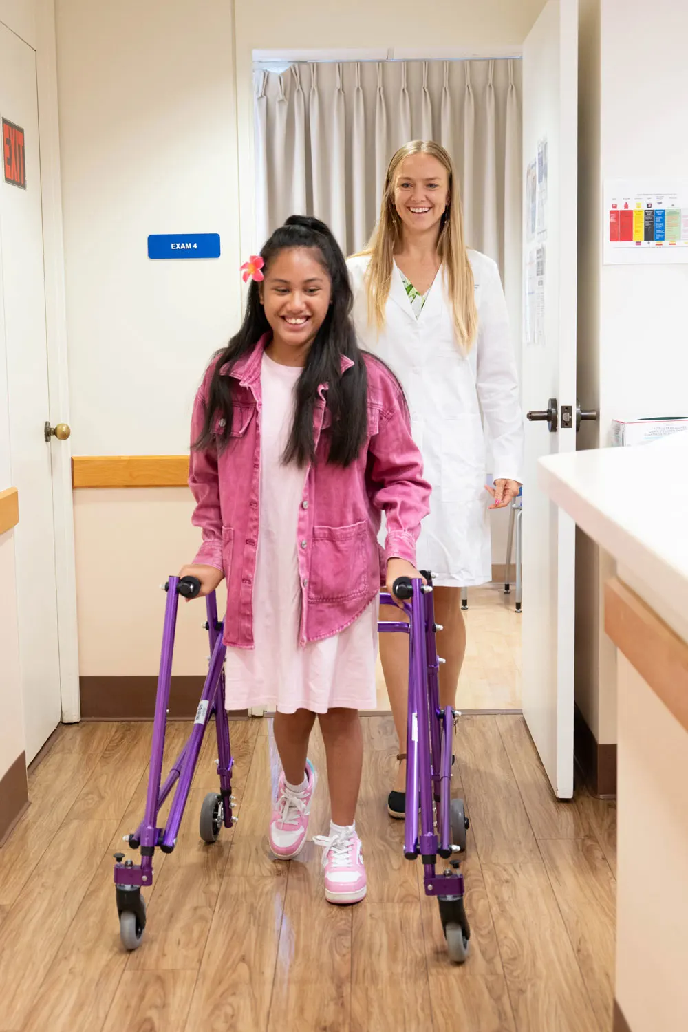 a doctor watches a child walk using an assistive device in an exam space