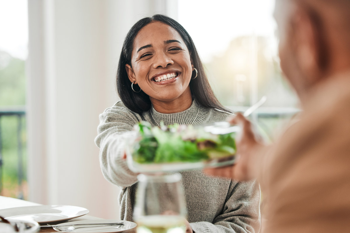 A woman smiles and passes the salad plate at a holiday dinner.
