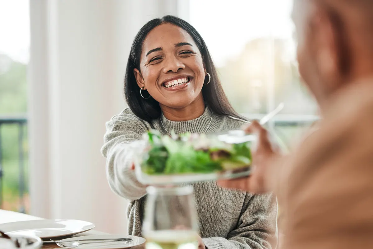 A woman smiles and passes the salad plate at a holiday dinner.