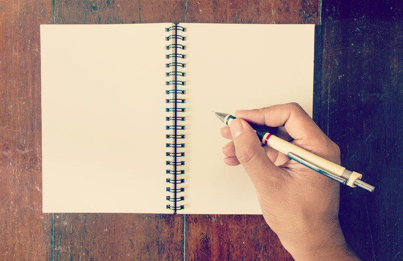 close up of a hand and pen above an empty notebook