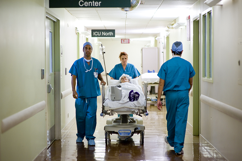 3 medical professionals rolling a patient in a bed down a hallway