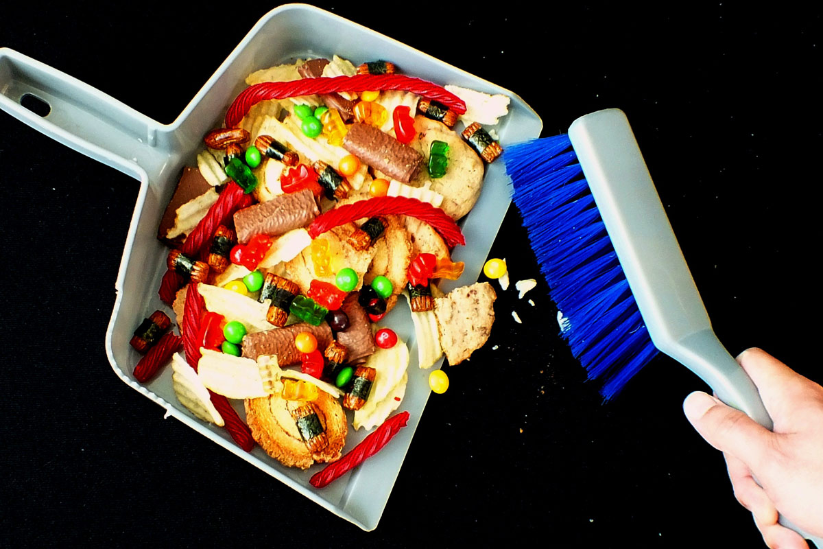 Person sweeping unhealthy candies, cookies and sweets into a dustpan