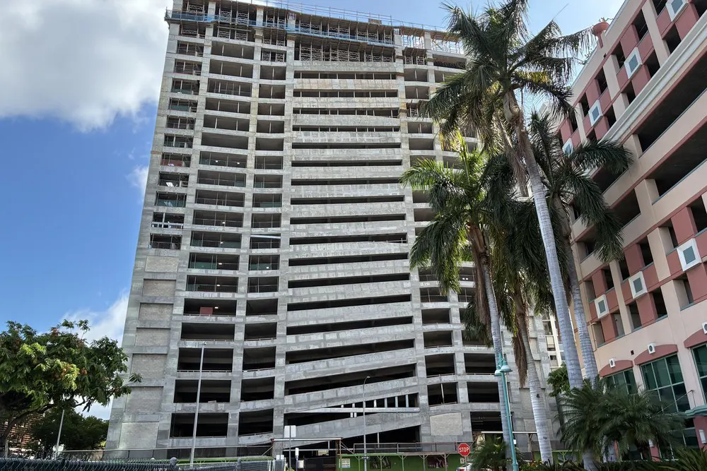 Front view of the parking building framed by palm trees and a neighboring structure.