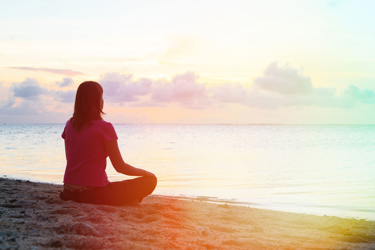 a lady on the beach sitting crossed legged during dawn