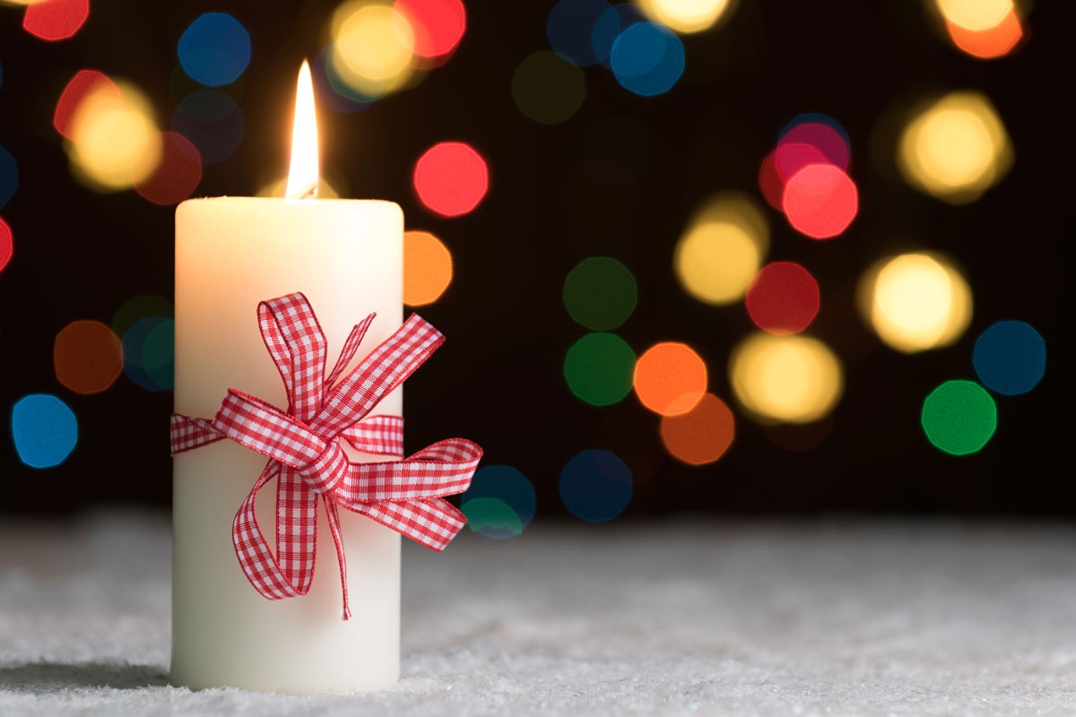 Candle with a bow around it and Christmas lights in the back